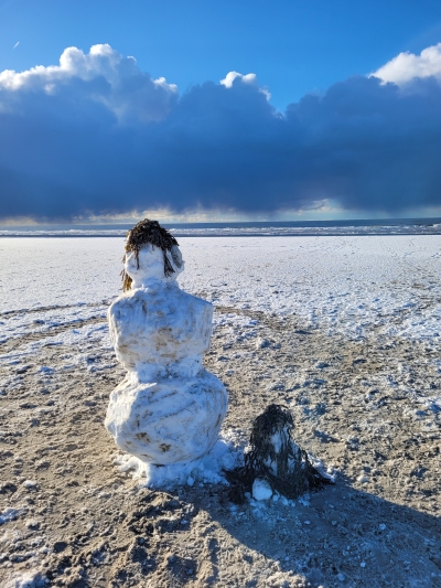 ein großer und ein kleiner Schneemann stehen am Stand von Amrum und blicken auf das Meer
